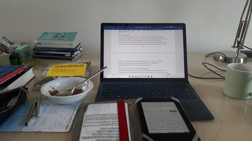 one of Monika Rinck's working tables: a laptop, a tablet, a bowl of cereals and texts